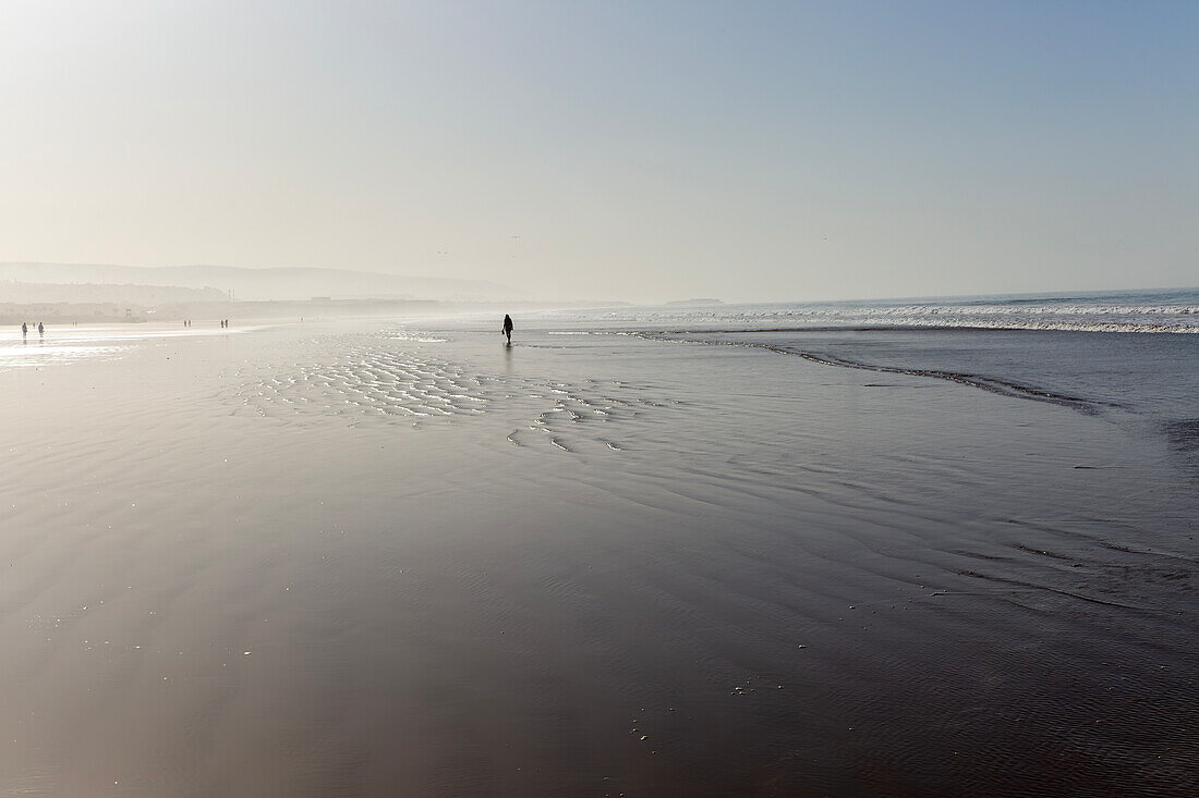 Silhouette von Menschen, die bei Ebbe am Strand spazieren, Taghazout, Marokko, Nordafrika