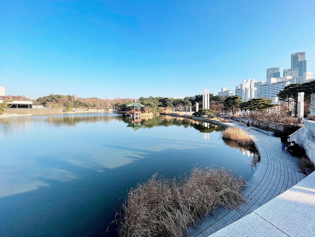  Lake in front of the National Museum, pagoda pavilion and urban skyscraper backdrop in winter sun, Seoul, South Korea, Asia 