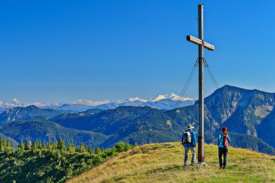  Man and woman hiking standing at the summit cross of Kratzer, Hohe Tauern in the background, Hirschberg, Bavarian Alps, Upper Bavaria, Bavaria, Germany 