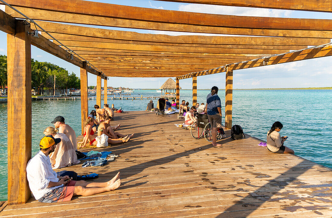 People sitting on woooden jetty pier by waterside, Lake Bacalar, Bacalar, Quintana Roo, Yucatan Peninsula, Mexico
