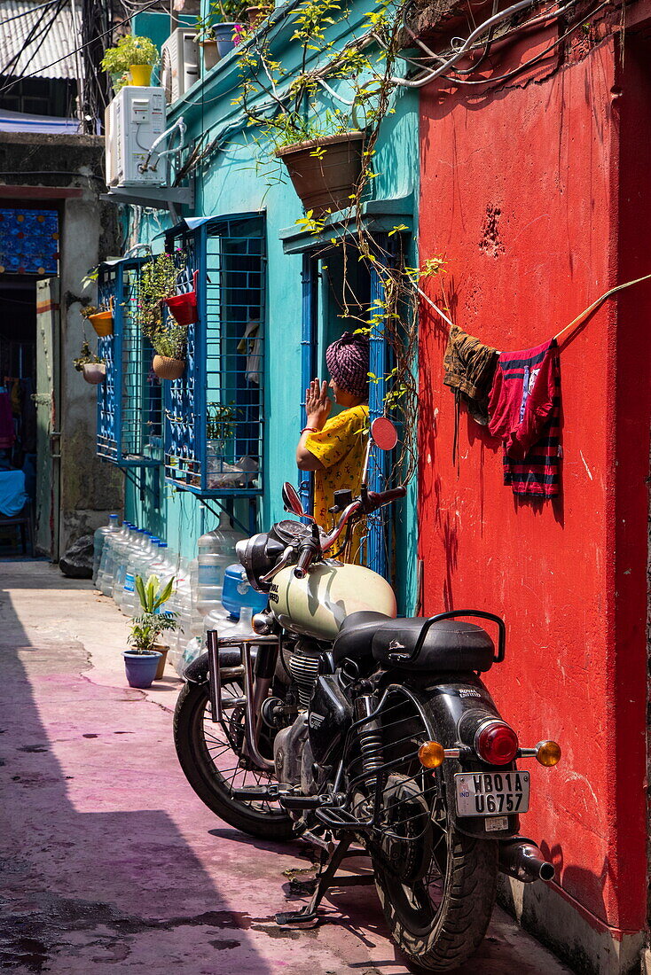 Frau betet in einer Gasse vor bunter Häuserzeile mit einem Motorrad im Vordergrund, im Bezirk Kumartuli, Kalkutta, Kalkutta, Indien, Asien