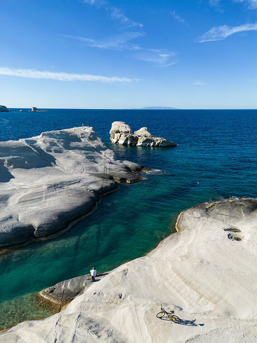  Aerial view of man with bicycle on Sarakiniko beach with its grey-white volcanic rock with bay and coastline, Sarakiniko, Milos, South Aegean, Greece, Europe 