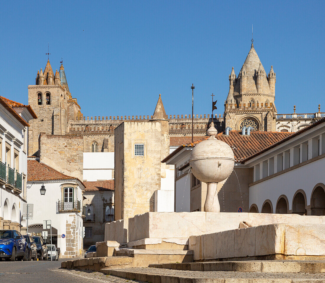 Fountain in the Largo das Portas de Moura with a view to the cathedral and surrounding historic buildings in the city centre of Evora, Alto Alentejo, Portugal, Southern Europe - 23 March 2019