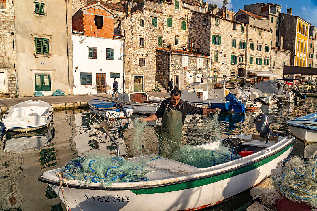 Fisherman with net on his boat at the small harbour of the old town in Sibenik, Croatia, Europe