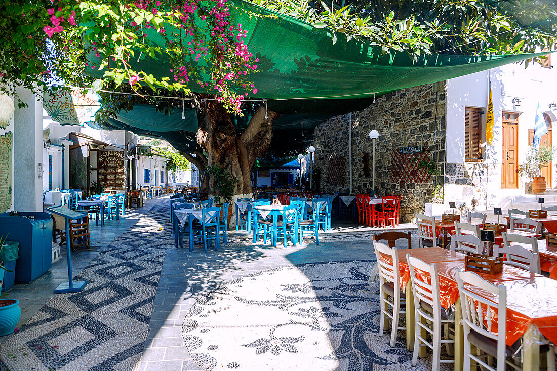 Dorfplatz Platía Ilikioméni mit Tavernen und Baumschatten in Mandráki auf der Insel Nissyros (Nisyros, Nissiros, Nisiros) in Griechenland