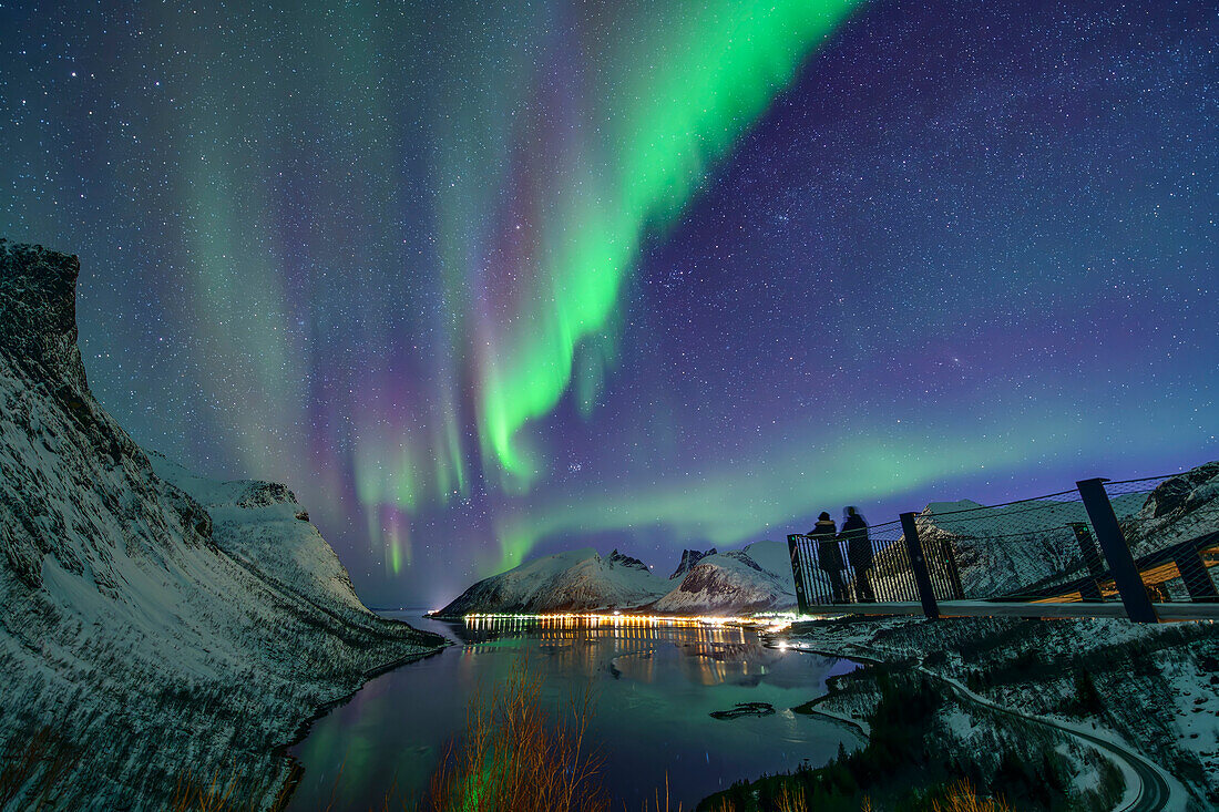  Two people standing on observation deck above the Nordfjord and looking at Northern Lights, Bergsbotn, Nordfjord, Senja, Troms, Norway 