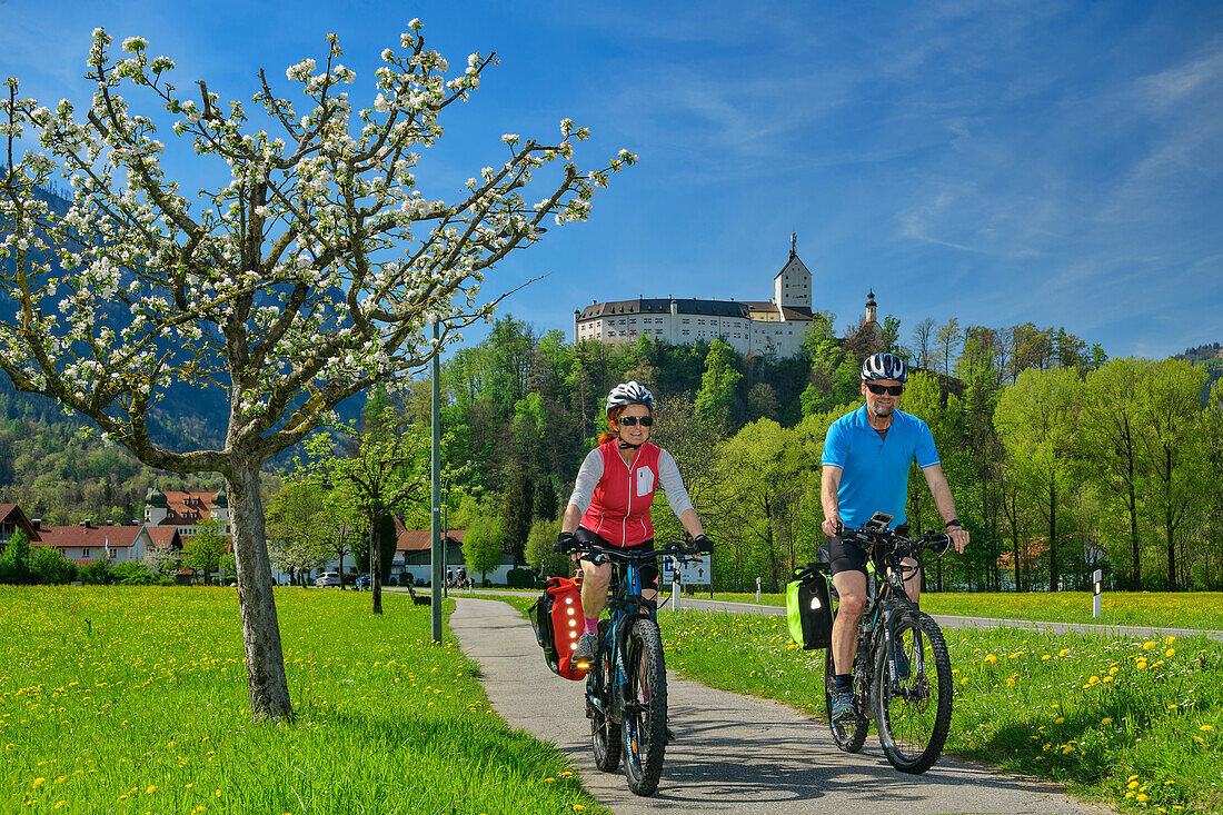 Mann und Frau beim Radfahren mit Schloss Hohenaschau im Hintergrund, Hohenaschau, Bodensee-Königssee-Radweg, Oberbayern, Bayern, Deutschland