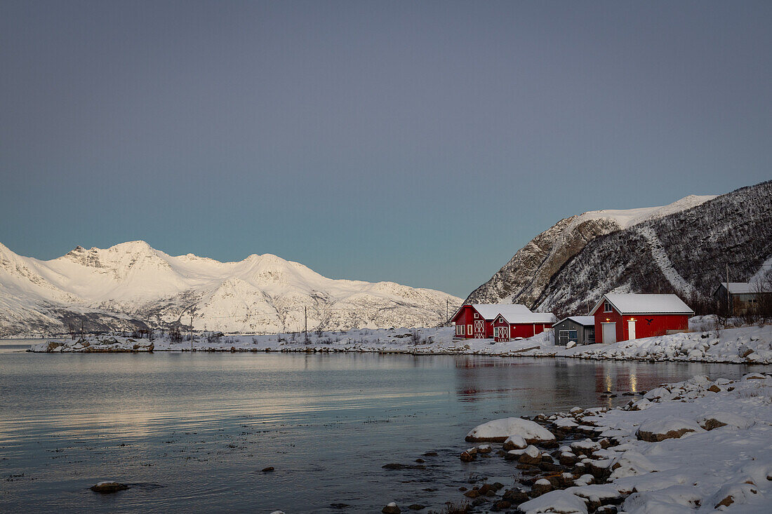 Winter in der Region Trömso, Tromvik, typisches traditionelles Haus mit Bergen im Dämmerungslicht