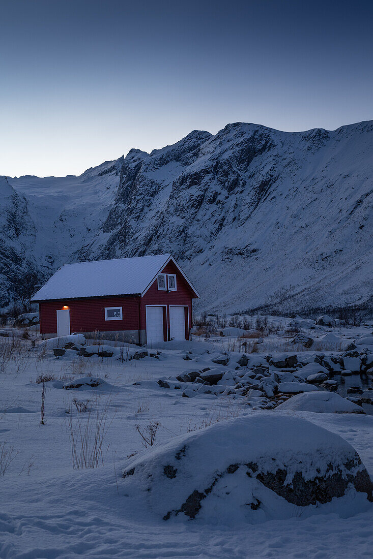 Winter in der Region Trömso, Tromvik, typisches traditionelles Haus mit Bergen im Dämmerungslicht