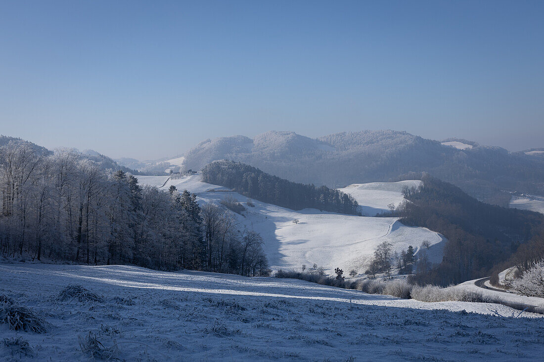 Winterlandschaft mit verschneiten Wiesen, Wäldern und Hügel im Jura (Aargau, Schweiz)