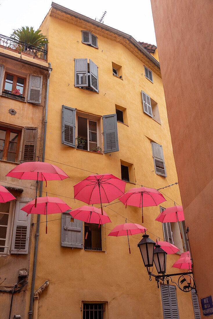  Red umbrellas hanging between yellow houses, perfume town Grasse, Provence-Alpes-Côte d&#39;Azur, France 