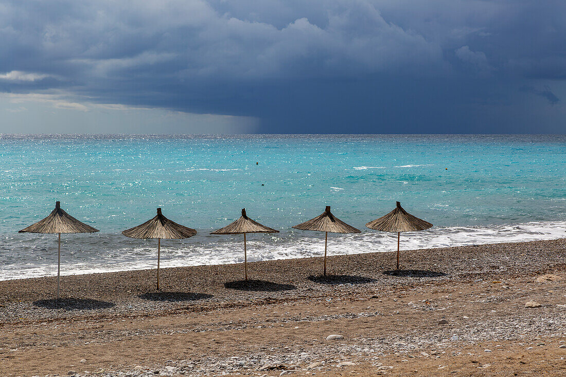 Line of sunshades along the beach with dark storm clouds offshore, Dhermi, Albania, Europe