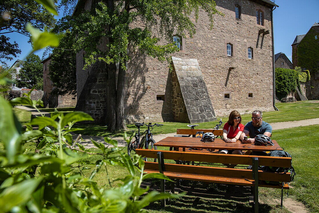 Two cyclists rest at picnic table in moat of Schloss Steinau palace, Steinau an der Straße, Spessart-Mainland, Hesse, Germany