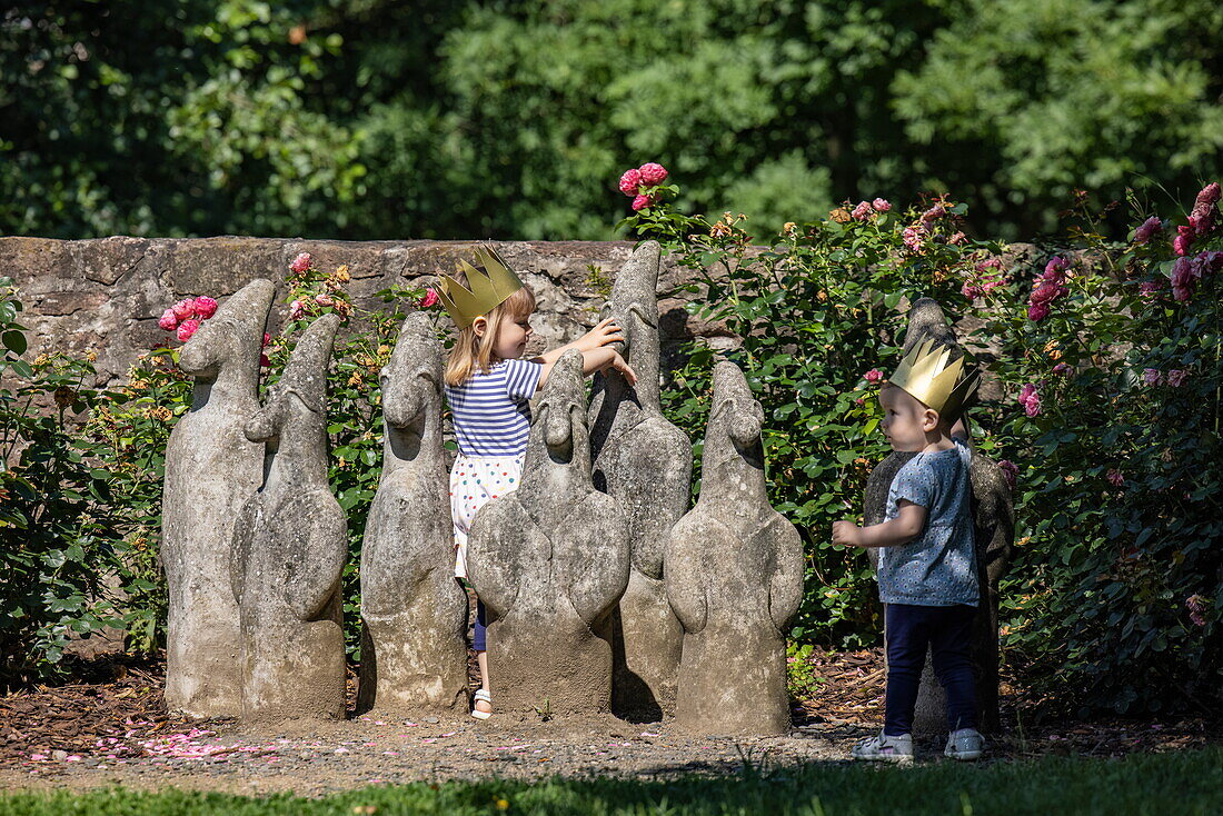 Zwei kleine Kinder mit goldenen Kronen spielen um die Statue die Sieben Zwerge im Garten des Brüder-Grimm-Hauses, Steinau an der Straße, Spessart-Mainland, Hessen, Deutschland