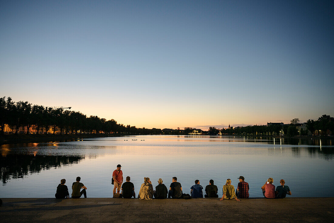 UNESCO Welterbe "Residenzensemble Schwerin", Menschen sitzen in der Dämmerung am Ufer des Pfaffenteich, Mecklenburg-Vorpommern, Deutschland, Europa