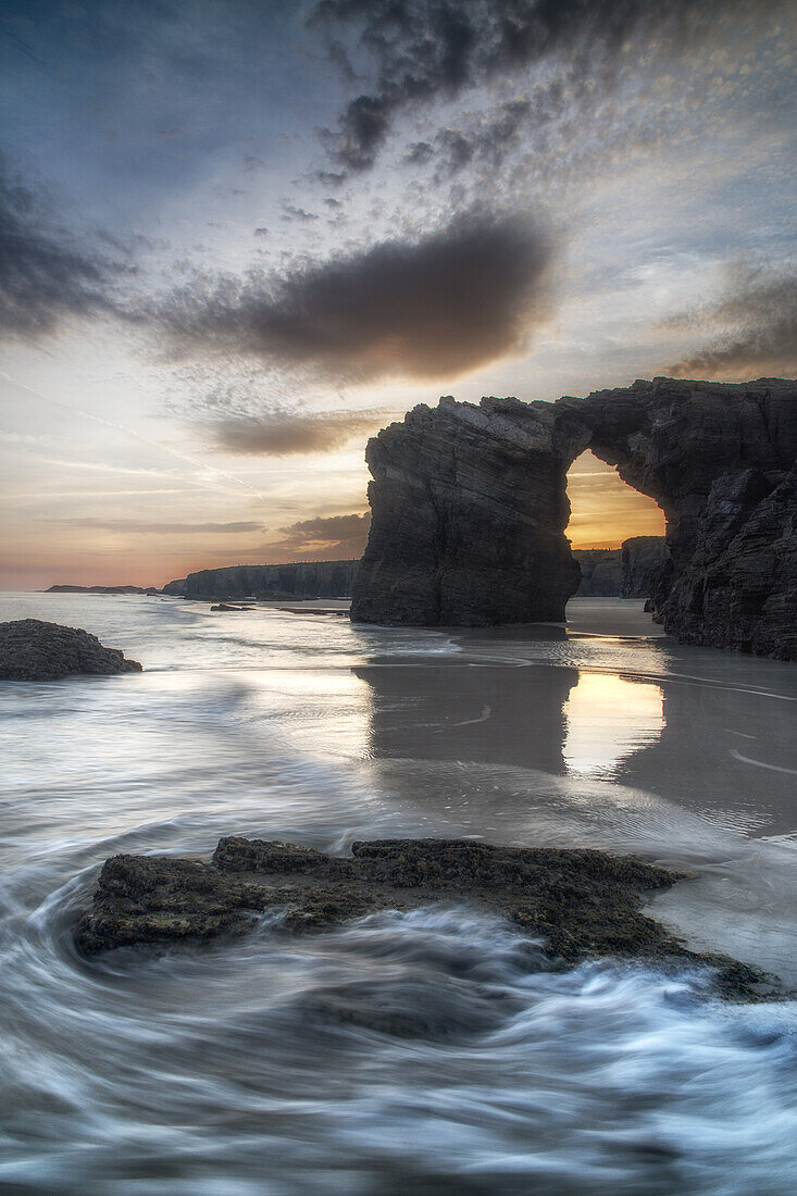 Blick durch einen Felsbogen am Sandstrand von Playa de las Catedralas bei Sonnenuntergang, Gemeinde Ribadeo, Provinz Lugo, Galicien, Nordspanien, Spanien