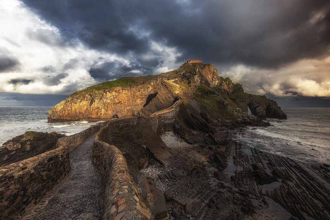  View of the path and the rocky island of San Juan de Gaztelugatxe under dark clouds. 