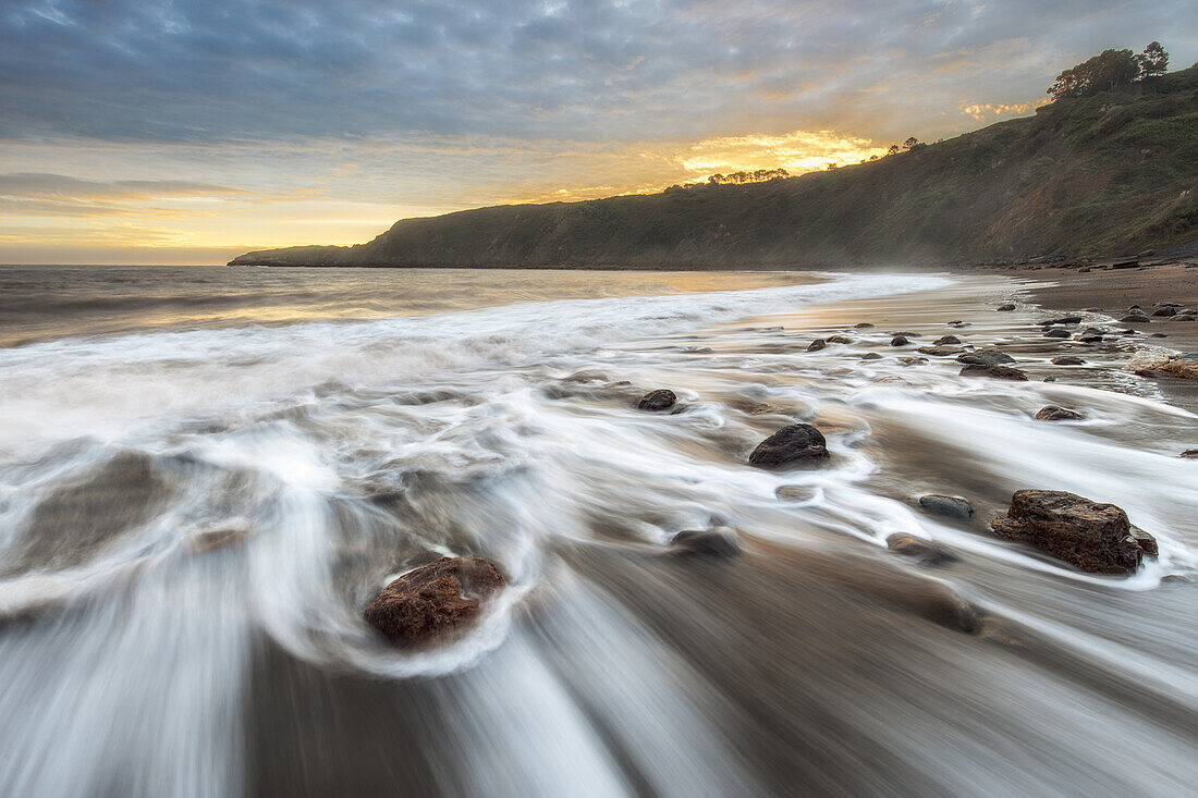  Traces of water wash over individual stones on the sandy beach. Golden sunset. 