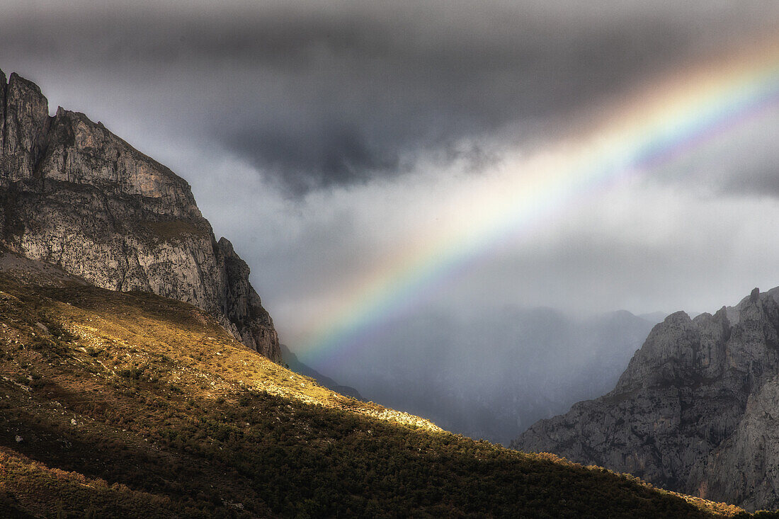  Rainbow in the mountains. Partial sunshine. Dark clouds. 