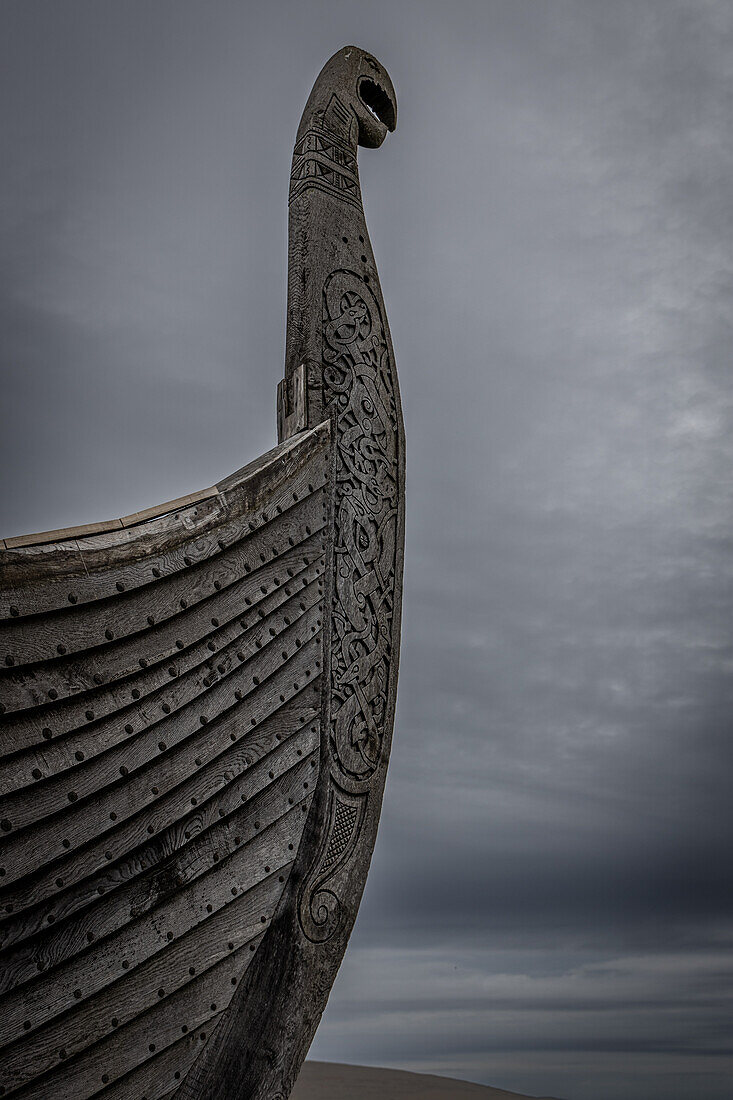  Bow of old Viking ship with dragon head against grey sky. 