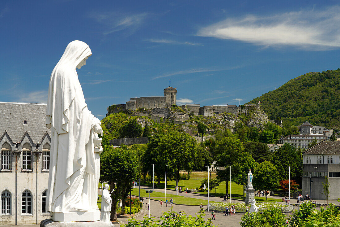 Statue auf dem Rosenkranz-Platz und die Festung Château fort de Lourdes im Marienwallfahrtsort Lourdes, Pyrenäen, Frankreich, Europa