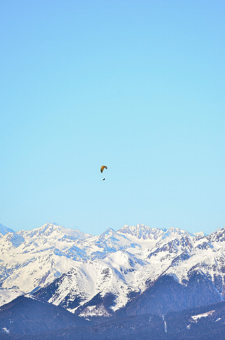 Gleitschirmflieger schwebt über dem Gipfel des K2 vor einem türkisfarbenen, pastellfarbenen Himmel.