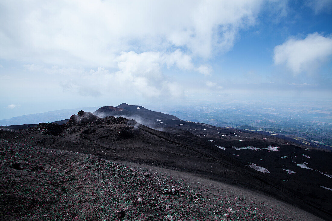 View of the summit of Mount Etna from the very top, featuring a blue sky.