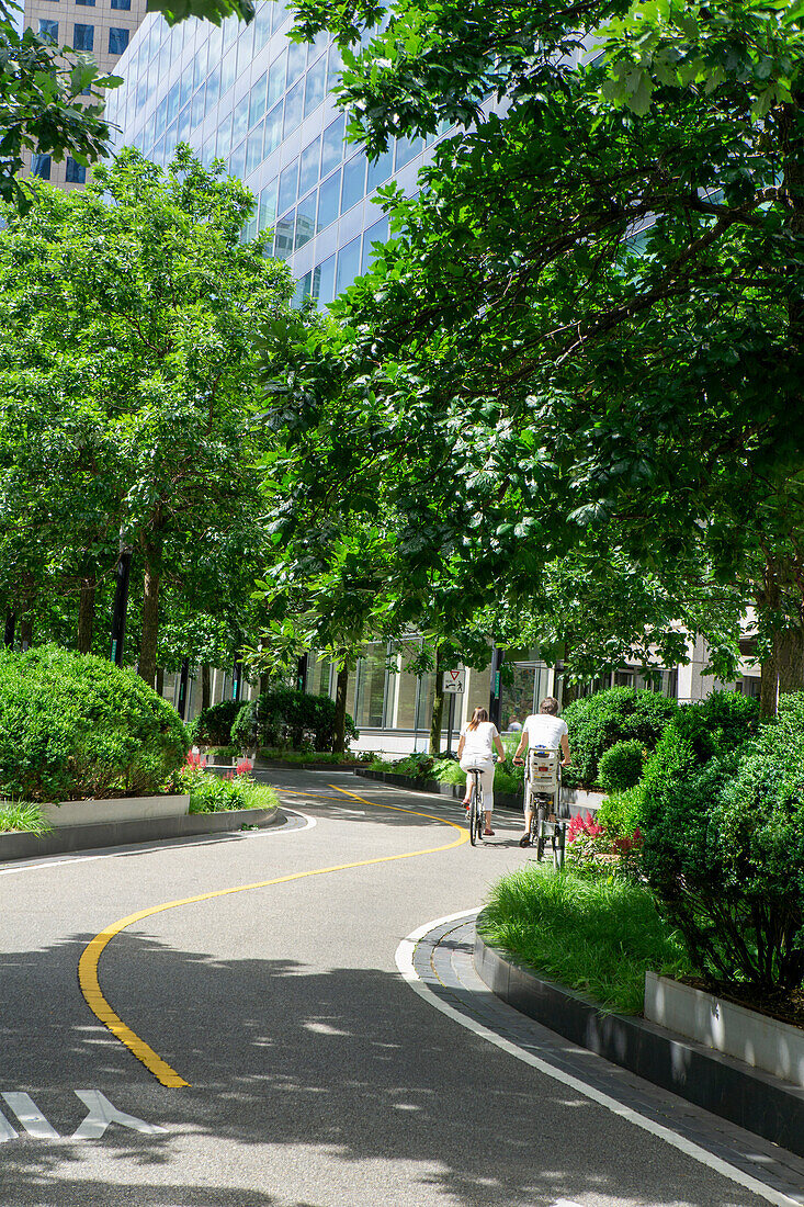 Rear view of couple, one with small child, riding bicycles on bicycle path with 200 West Street in background, New York City, New York, USA