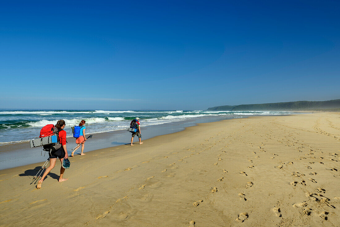 Drei Personen wandern über den Sandstrand von Nature's Valley, Otter Trail, Tsitsikamma Section, Garden Route National Park, Eastern Cape, Südafrika