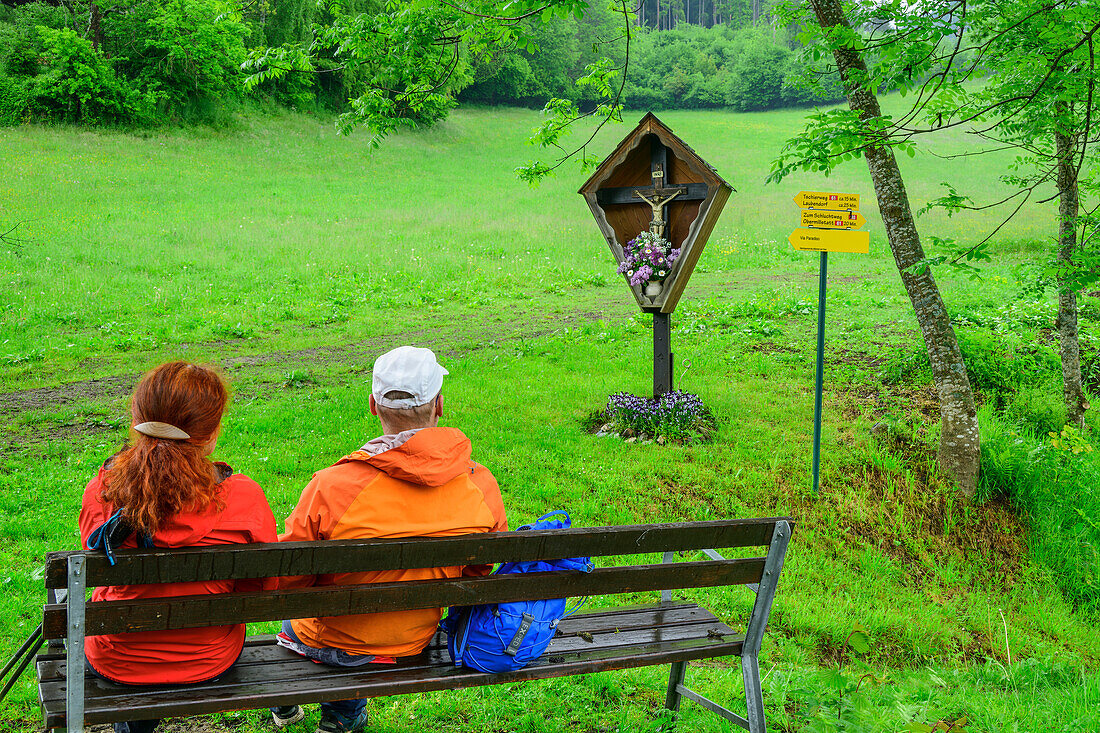 Mann und Frau machen auf Bank Pause, Wegkreuz im Hintergrund, Via paradiso, Millstätter See, Nockberge, Niedere Tauern, Kärnten, Österreich