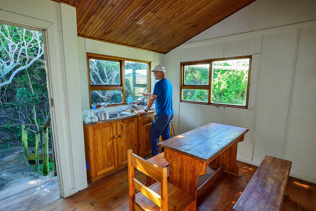 Mann arbeitet in Küche einer Selbstversorgerhütte auf dem Alexandria Hiking Trail, Woody Cape Hut, Addo Elephant National Park, Eastern Cape, Südafrika