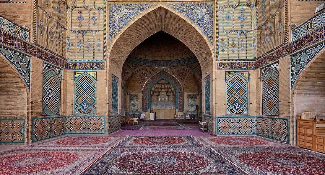 Panoramic interior view of the Hakim Mosque with ornate tiled mosaics on its brick walls and carpeted floor. Isfahan, Iran.