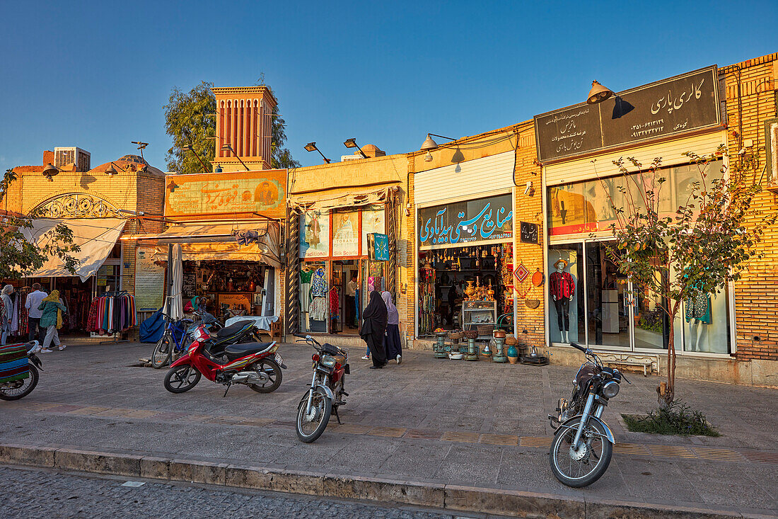 Sonnenbeschienene Fassaden zahlreicher Souvenirläden entlang der Masjed Jame, Straße im historischen Zentrum von Yazd, Iran.