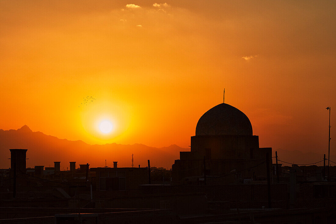 Silhouette traditionelles Kuppelgebäude vor der untergehenden Sonne und dem orangefarbenen Abendhimmel. Yazd, Iran.