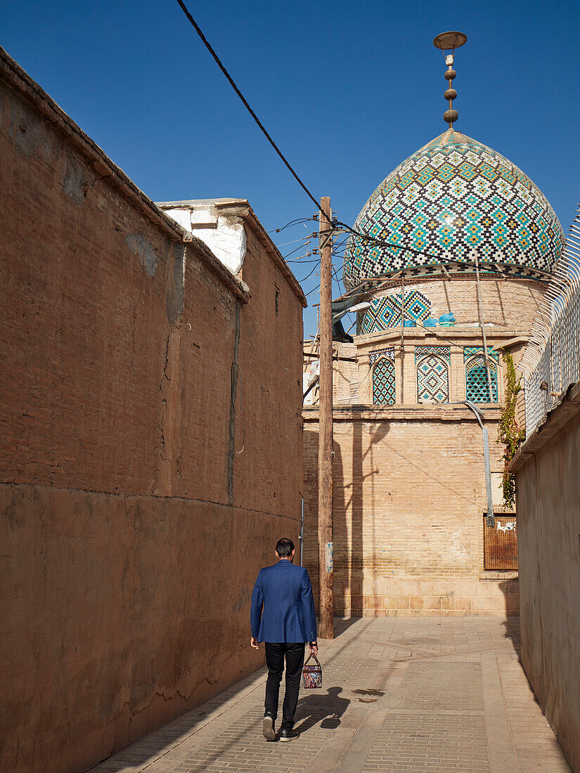 A man walks in a narrow street towards the 19th century Nasir al-Mulk Mosque, aka the Pink Mosque. Shiraz, Iran.