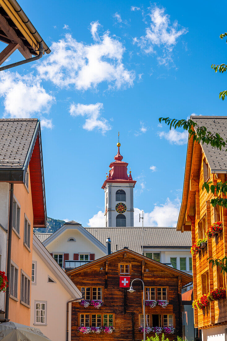 Altstadt mit Holzhaus und Kirchturm an einem sonnigen Sommertag in Andermatt, Uri, Schweiz.