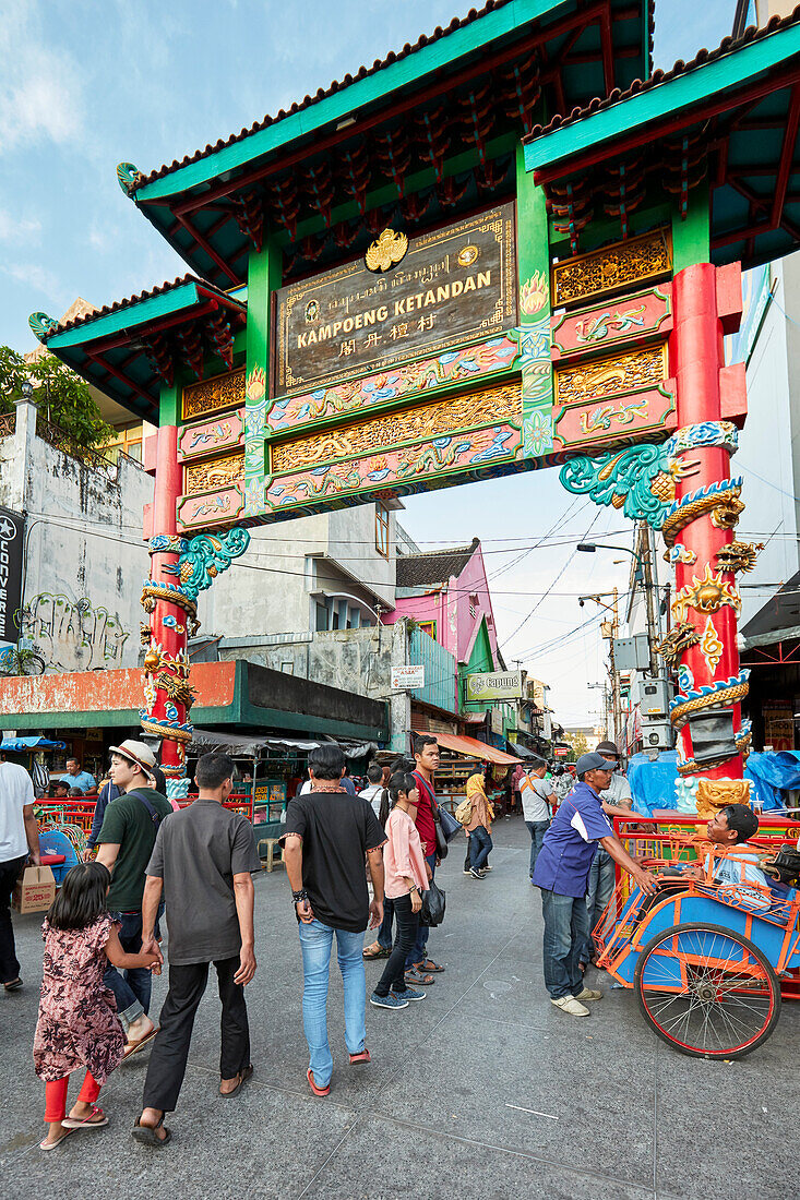 Menschen gehen durch das kunstvolle Eingangstor zum Bezirk Kentandan an der Ecke der Straßen Malioboro und Ketandan Wetan. Yogyakarta, Java, Indonesien.