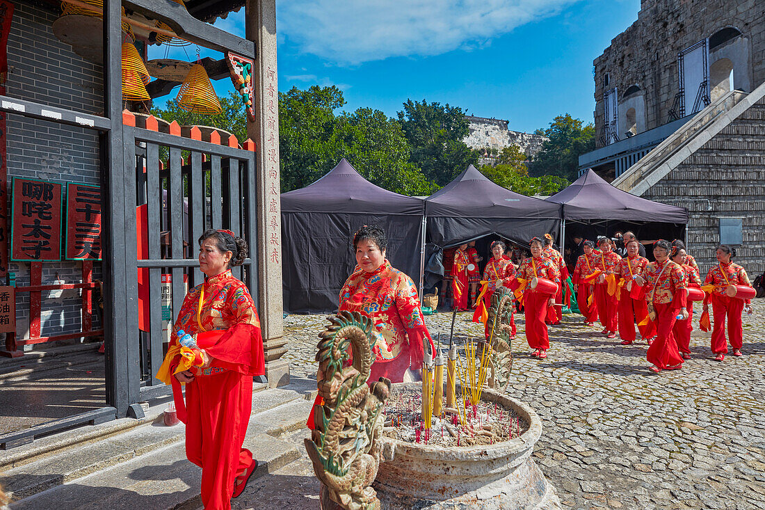  Einheimische Frauen in traditionellen roten Kostümen gehen am Na Tcha-Tempel vorbei. Macau, China. 