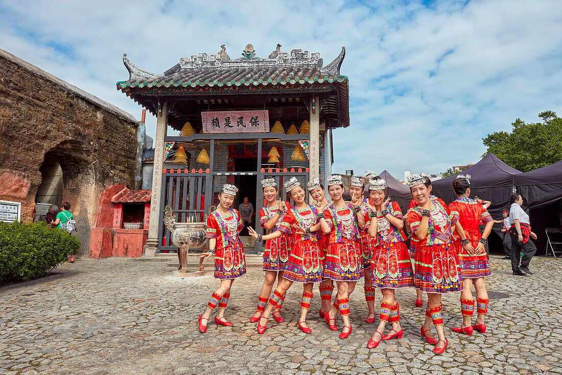 Local girls wearing red traditional costumes poses in front of the Na Tcha Temple. Macau, China.