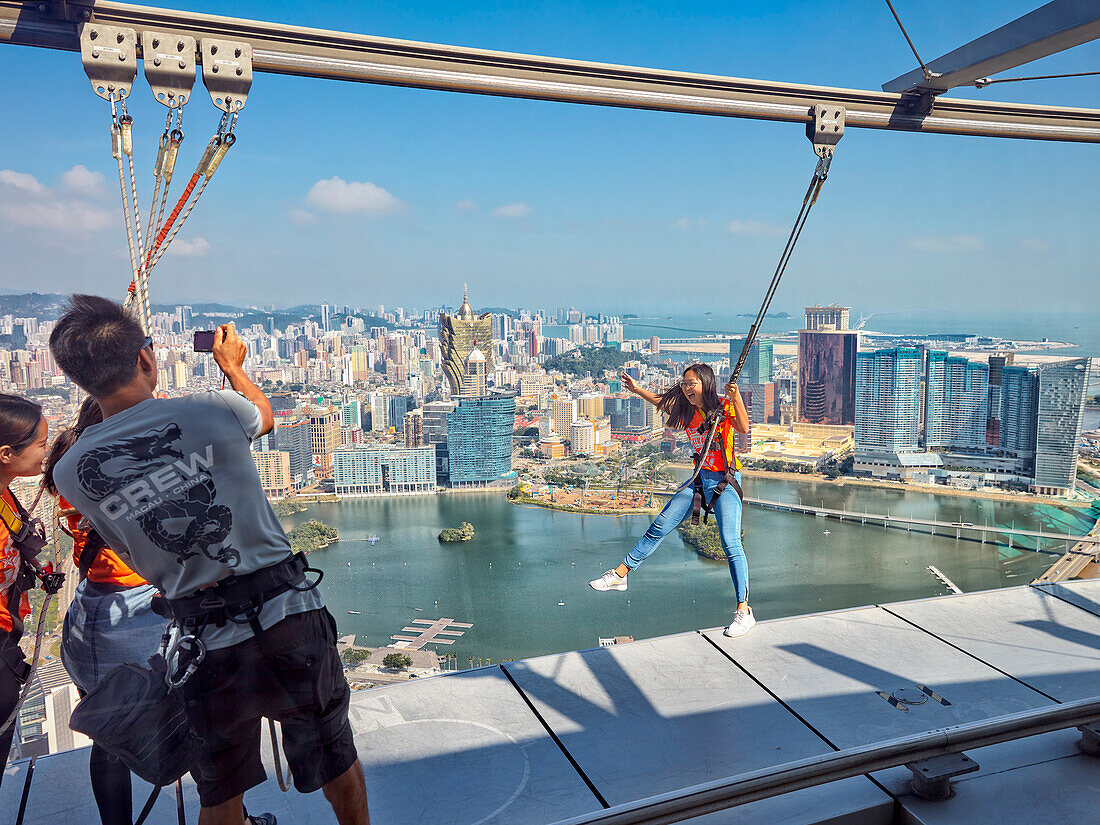 Frau posiert für ein Foto, während es um den äußeren Bereich des Macau Tower herumläuft. Macau, China.