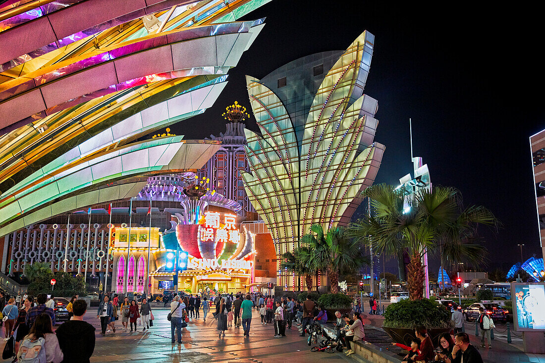 People walk at the Grand Lisboa Hotel and Casino brightly illuminated at night. Macau, China.