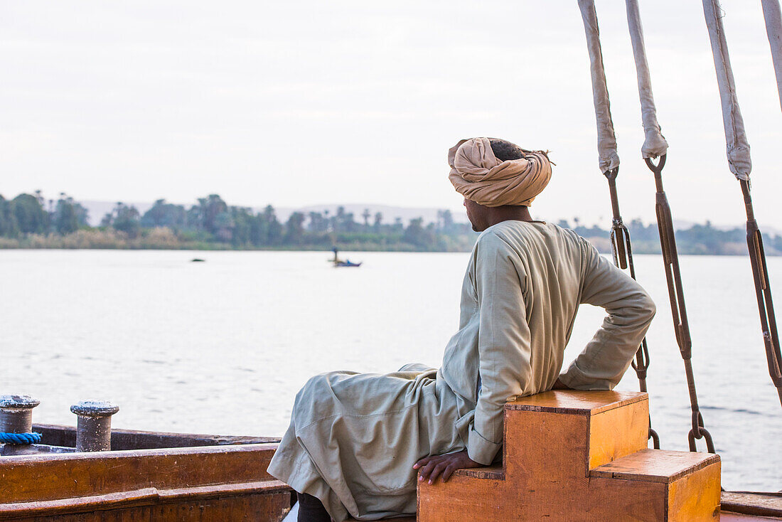 Member of the crew sitting at the prow of a dahabeah, passenger river boat of the Lazuli fleet, sailing on the Nile river, Egypt, northeast Africa