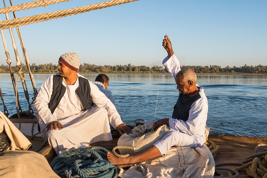 Members of the crew sitting at the prow of a dahabeah, passenger river boat of the Lazuli fleet, sailing on the Nile river, Egypt, northeast Africa