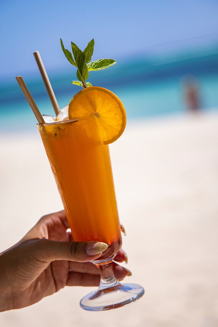 Fruchtcocktail in der Hand einer Frau am Strand, Le Morne, Rivière Noire, Insel Mauritius, Indischer Ozean