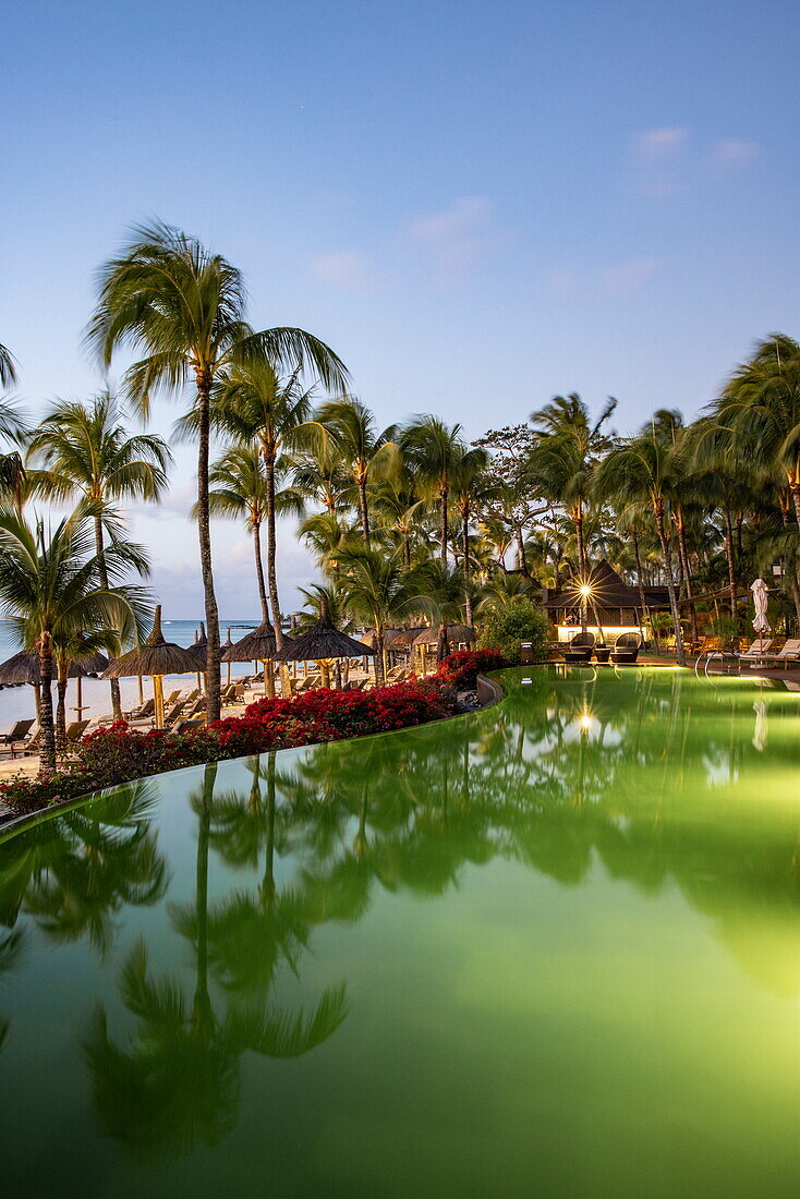  Swimming pool and thatched umbrellas with coconut palms at Royal Palms Beachcomber Luxury (Beachcomber Resorts) at dusk, Grand Baie, Rivière du Rempart, Mauritius, Indian Ocean 