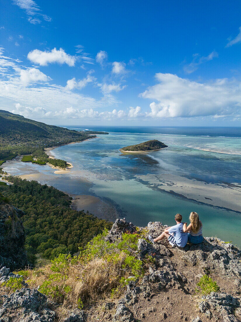  Aerial view of couple enjoying view over lagoon and coast halfway through hike up Le Morne mountain, Le Morne, Rivière Noire, Mauritius, Indian Ocean 