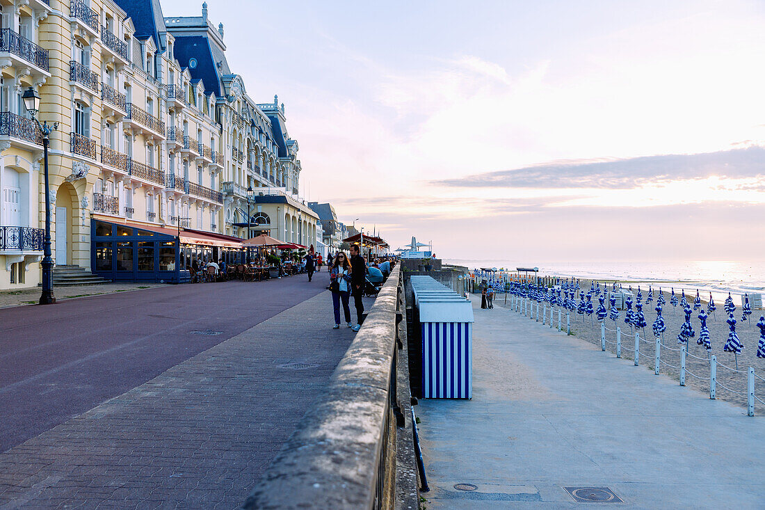  Beach promenade (Promenade Marcel Proust) with Grand Hotel (Le Grand Hôtel) and casino, bathing huts and folded umbrellas on the beach at sunset in the evening light in Cabourg on the Flower Coast (Côte Fleurie, Cote Fleurie) in the Calvados department in the Normandy region of France 