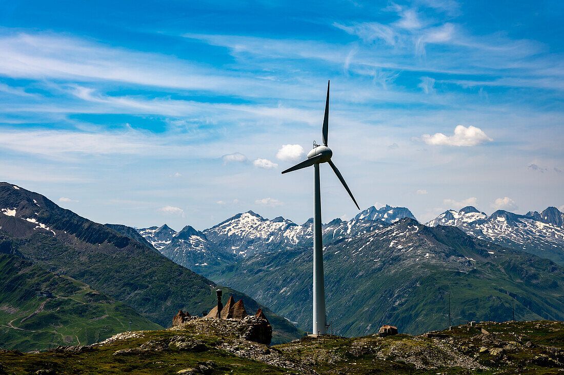  Windrad und Berg mit Gletscher vor blauem Himmel und Wolken an einem sonnigen Sommertag in Andermatt, Uri, Schweiz. 