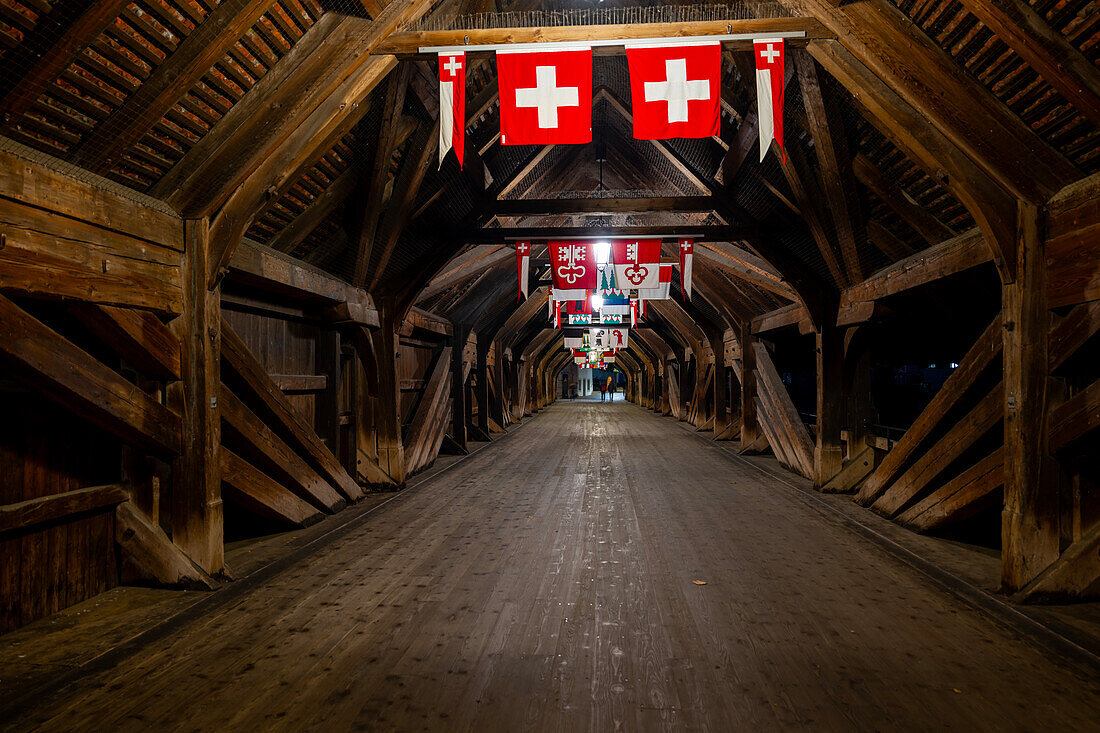 Inside the Old Historical Covered Wood Bridge Holzbrücke with Flags over River Aare at Night in Olten, Canton Solothurn, Switzerland.