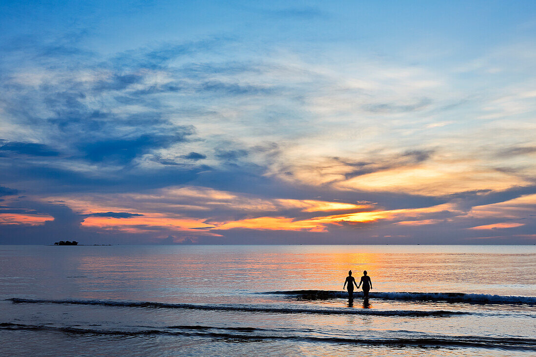  Zwei Mädchen waten bei Sonnenuntergang ins Meer. Insel Phu Quoc, Vietnam. 